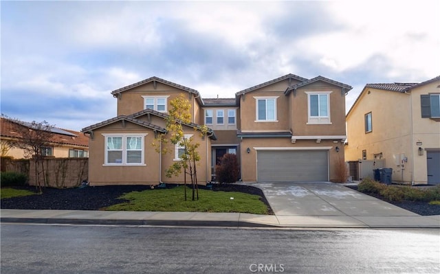 view of front of home with concrete driveway, an attached garage, fence, and stucco siding