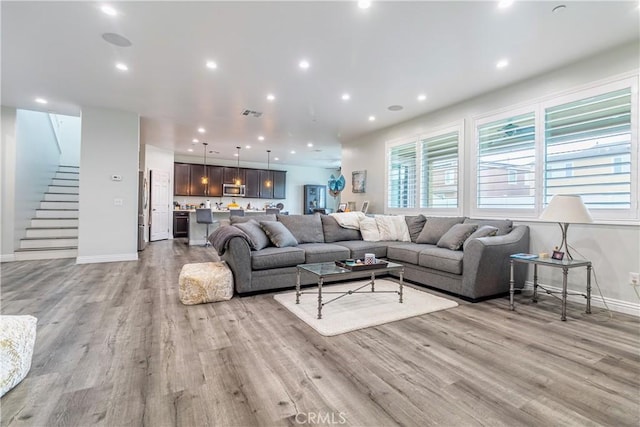 living area featuring recessed lighting, baseboards, stairs, and light wood finished floors