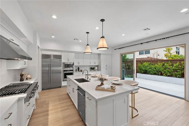 kitchen with visible vents, light wood-style flooring, a sink, white cabinets, and built in appliances