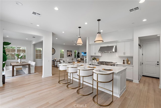 kitchen featuring under cabinet range hood, visible vents, a breakfast bar, and a sink