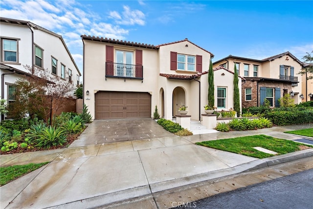 mediterranean / spanish home with stucco siding, a tile roof, concrete driveway, an attached garage, and a balcony