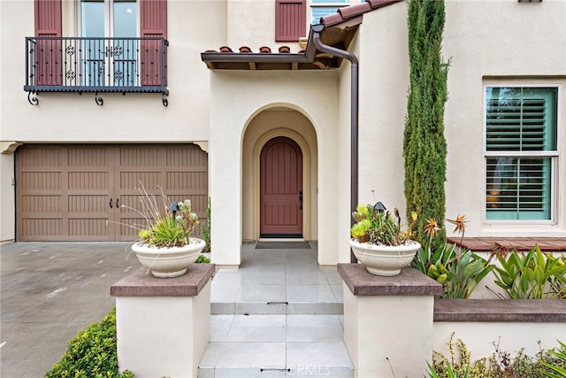 entrance to property featuring aphalt driveway, a balcony, an attached garage, and stucco siding