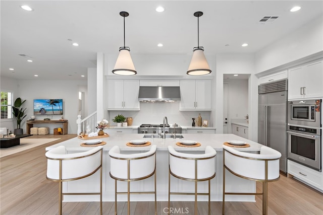 kitchen featuring visible vents, under cabinet range hood, built in appliances, light countertops, and a sink