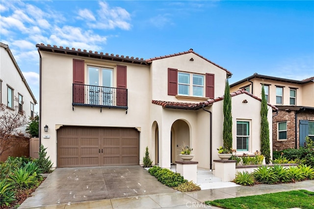 mediterranean / spanish-style home with stucco siding, a tile roof, concrete driveway, an attached garage, and a balcony