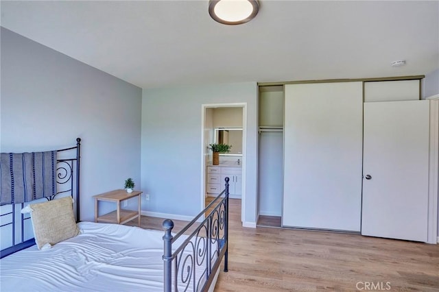 bedroom with light wood-type flooring, baseboards, a closet, and ensuite bath