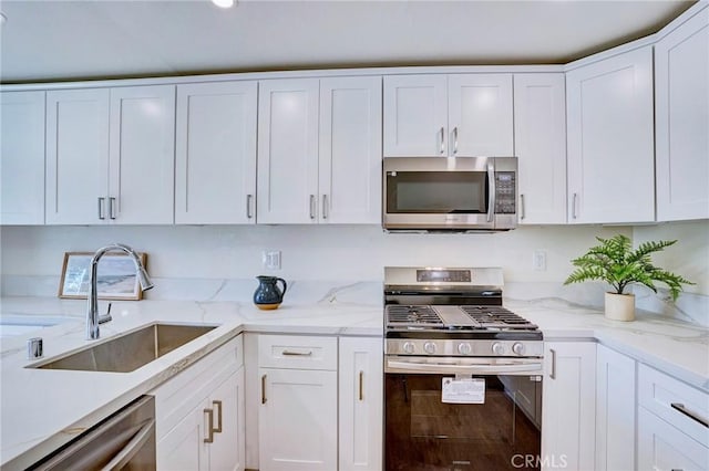 kitchen with white cabinets, light stone countertops, stainless steel appliances, and a sink