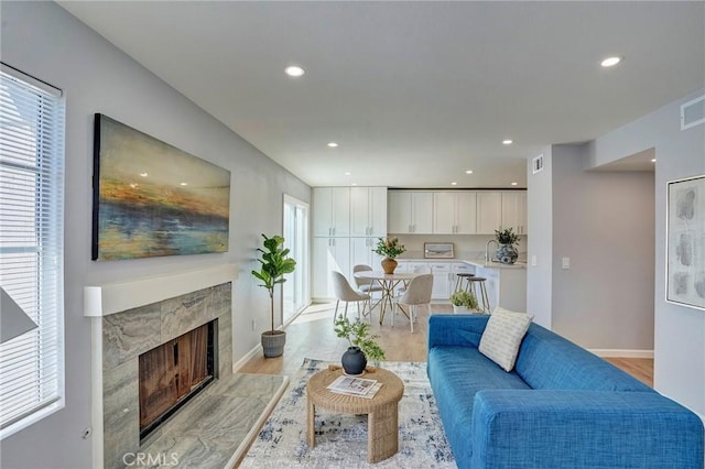 living area featuring a high end fireplace, visible vents, recessed lighting, and light wood finished floors