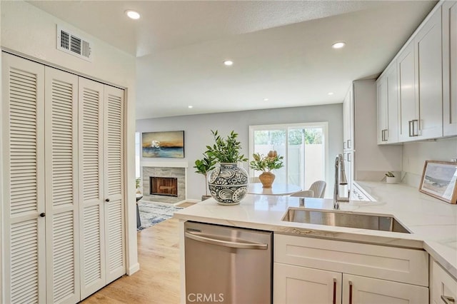 kitchen featuring visible vents, a sink, a peninsula, light countertops, and dishwasher