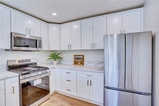 kitchen featuring light stone counters, appliances with stainless steel finishes, light wood-style flooring, and white cabinetry