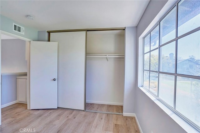 unfurnished bedroom with a closet, visible vents, baseboards, and wood finished floors