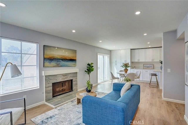 living room featuring a high end fireplace, recessed lighting, light wood-style flooring, and baseboards