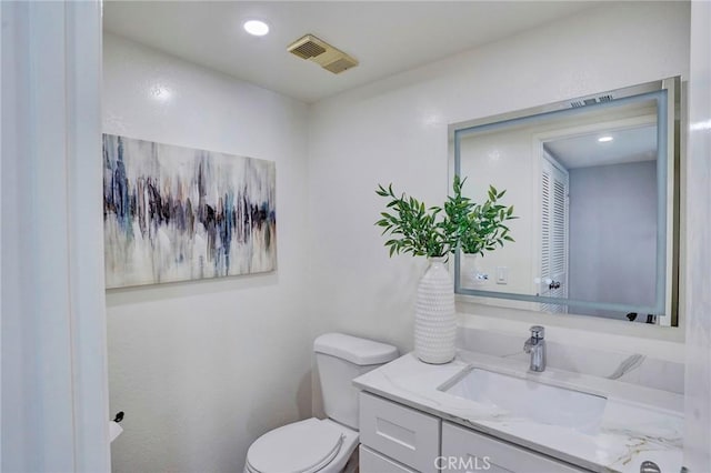 half bath with visible vents, recessed lighting, toilet, and vanity