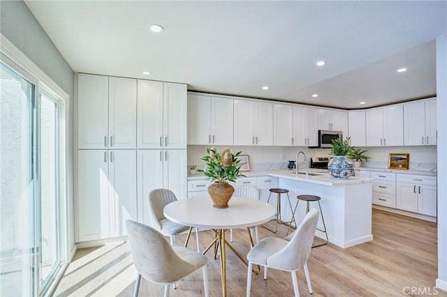 kitchen with light wood finished floors, stainless steel microwave, white cabinetry, recessed lighting, and light countertops