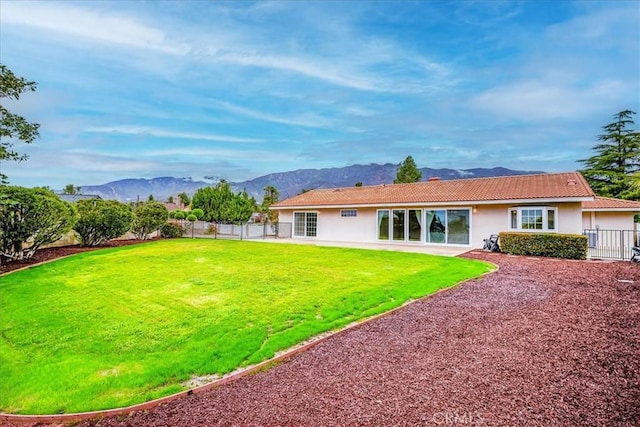 rear view of house featuring fence, a yard, stucco siding, a tile roof, and a mountain view