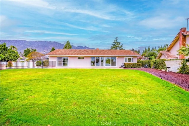 back of house with stucco siding, a mountain view, a yard, and fence