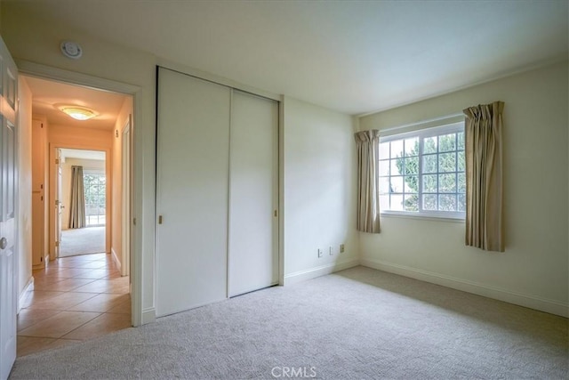 unfurnished bedroom with multiple windows, a closet, light tile patterned floors, and light carpet