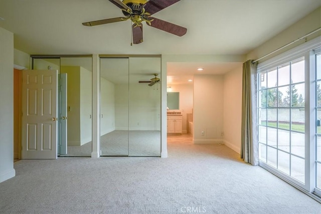 unfurnished bedroom with baseboards, ensuite bath, ceiling fan, multiple closets, and carpet flooring