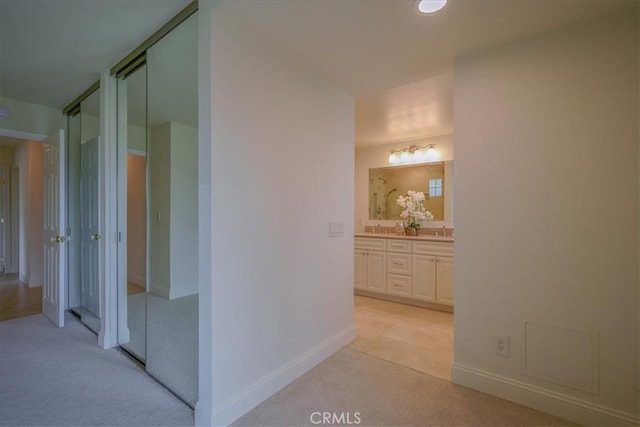 corridor with light colored carpet, baseboards, and a sink