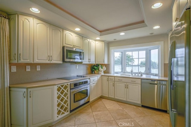 kitchen featuring a tray ceiling, a sink, ornamental molding, light countertops, and appliances with stainless steel finishes