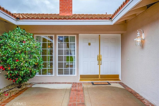 doorway to property featuring stucco siding, a tiled roof, and a chimney