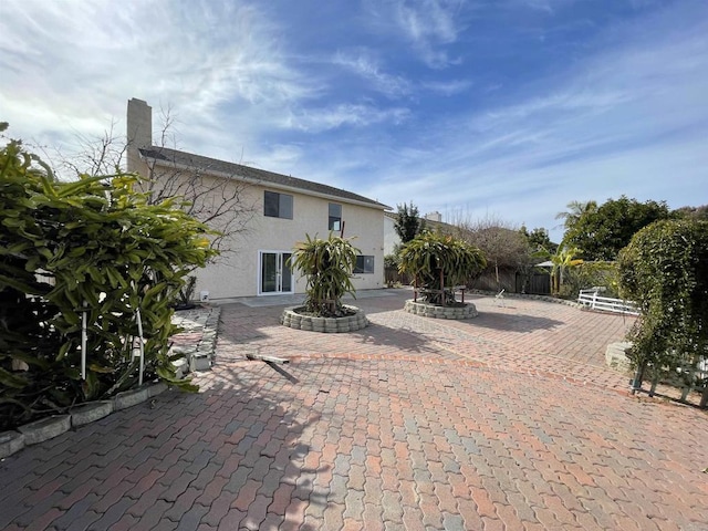 exterior space featuring stucco siding, a chimney, a patio, and fence