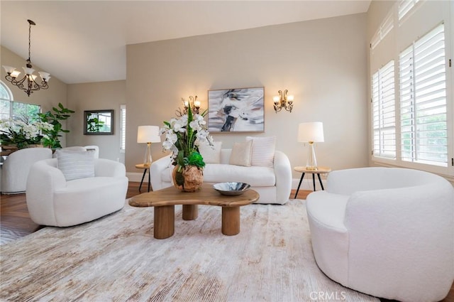 living area featuring an inviting chandelier, wood finished floors, baseboards, and vaulted ceiling