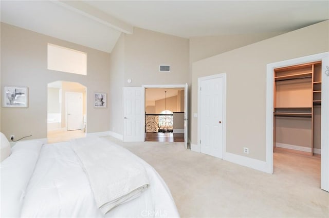 bedroom with a walk in closet, light carpet, beam ceiling, high vaulted ceiling, and arched walkways