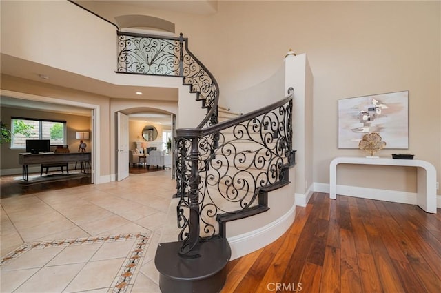 staircase featuring baseboards, arched walkways, and a high ceiling