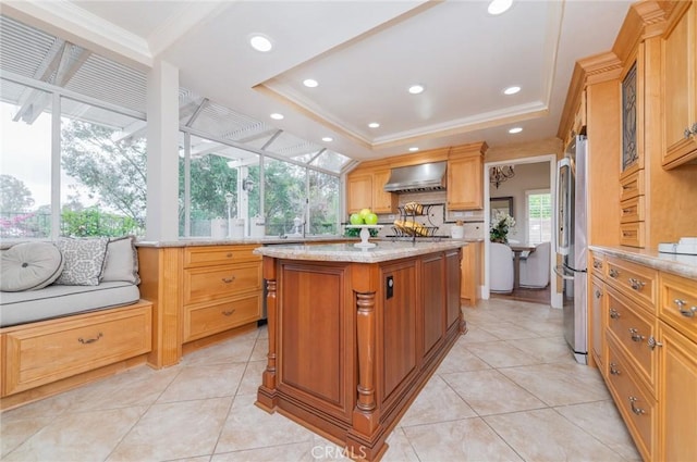 kitchen with light stone counters, a center island, freestanding refrigerator, wall chimney exhaust hood, and a raised ceiling