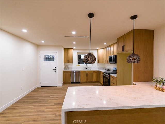 kitchen with brown cabinets, appliances with stainless steel finishes, light wood-type flooring, and light stone countertops