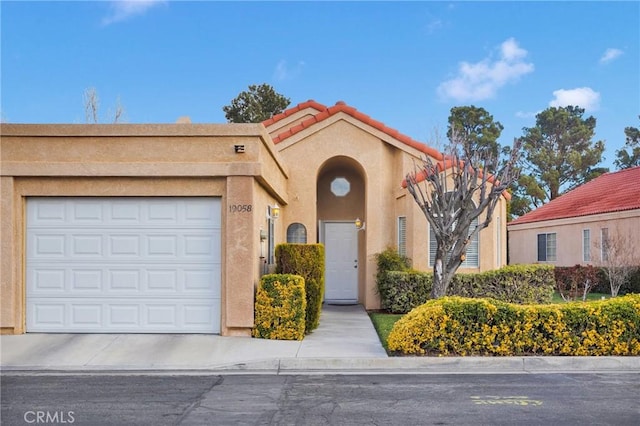 mediterranean / spanish home featuring stucco siding, a tiled roof, and an attached garage