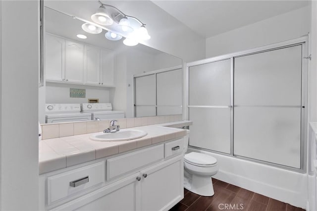 full bathroom with wood tiled floor, toilet, washing machine and dryer, combined bath / shower with glass door, and vanity