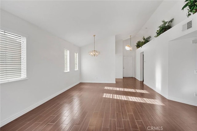 empty room with visible vents, baseboards, a chandelier, vaulted ceiling, and wood finished floors