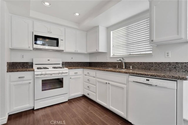 kitchen with white appliances, dark wood-style floors, a tray ceiling, a sink, and white cabinetry