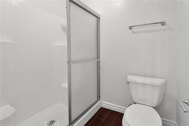 bathroom featuring baseboards, wood finished floors, toilet, and a stall shower