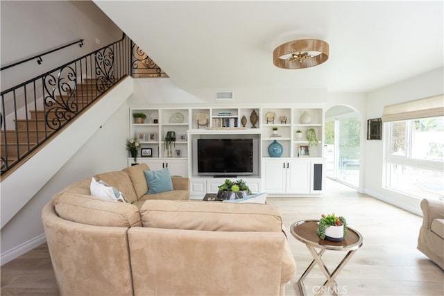 living room featuring visible vents, arched walkways, light wood finished floors, baseboards, and stairs