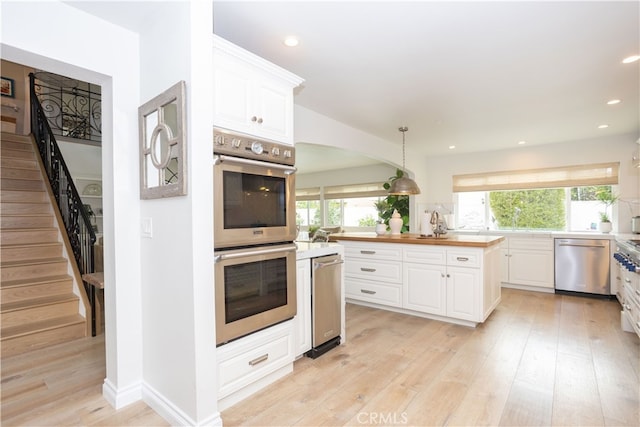 kitchen with a wealth of natural light, white cabinets, appliances with stainless steel finishes, and light wood-type flooring