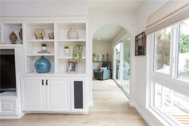 hallway featuring light wood-style flooring, baseboards, and arched walkways