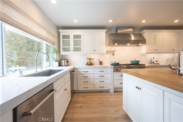 kitchen featuring white cabinets, wall chimney exhaust hood, appliances with stainless steel finishes, and a sink