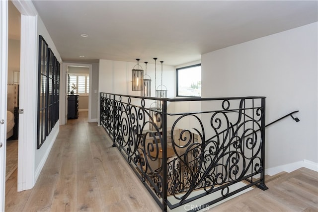 corridor featuring baseboards, an upstairs landing, a healthy amount of sunlight, and wood finished floors