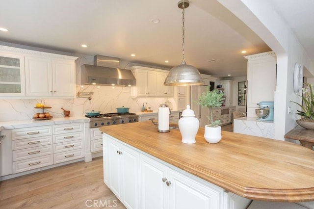 kitchen featuring light wood finished floors, stainless steel gas stovetop, arched walkways, white cabinetry, and wall chimney exhaust hood