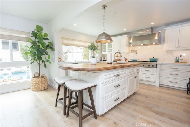 kitchen featuring a sink, wooden counters, backsplash, and wall chimney range hood