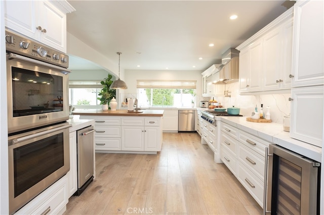 kitchen with light wood-style flooring, beverage cooler, custom range hood, stainless steel appliances, and white cabinets