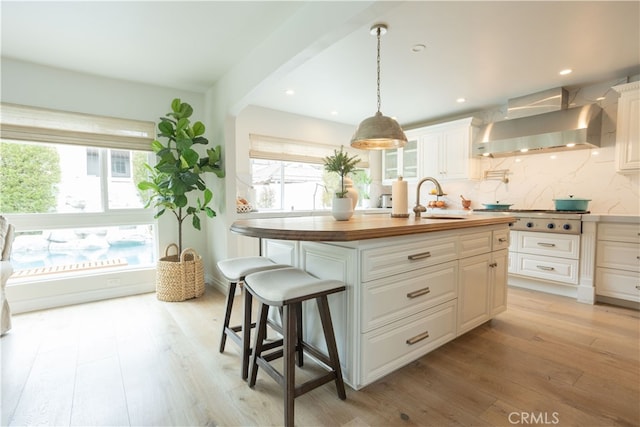 kitchen featuring butcher block counters, light wood-type flooring, wall chimney range hood, and a sink