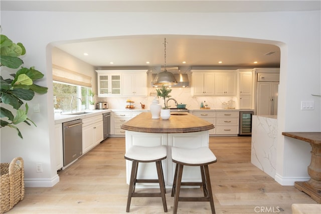 kitchen featuring beverage cooler, butcher block countertops, an island with sink, stainless steel dishwasher, and a sink