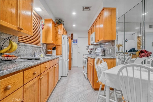 kitchen featuring decorative backsplash, white appliances, light stone counters, and visible vents