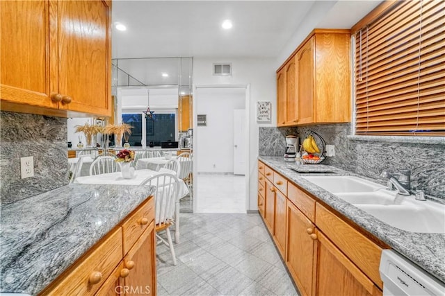 kitchen with visible vents, backsplash, light stone counters, white dishwasher, and a sink