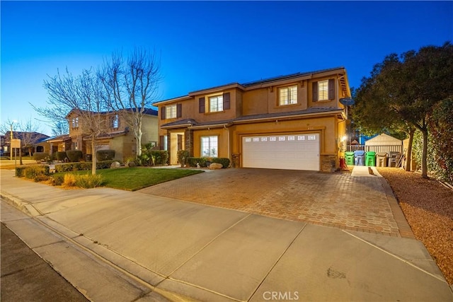 view of front facade featuring an attached garage, stucco siding, a front lawn, decorative driveway, and roof mounted solar panels