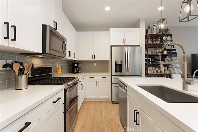 kitchen featuring light wood-type flooring, a sink, backsplash, appliances with stainless steel finishes, and light countertops