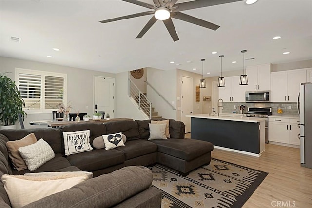 living room with visible vents, light wood-style flooring, recessed lighting, ceiling fan, and stairs